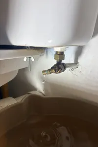 Robinet d’alimentation sous un réservoir de toilettes, avec un bac placé dessous.